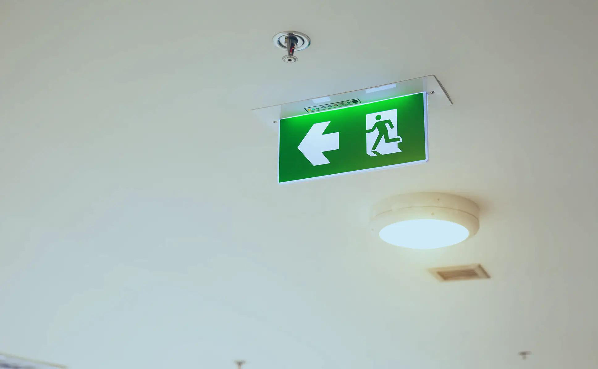 Emergency Lighting & Central Battery close-up-green-emergency-fire-exit-sign-building-ceiling